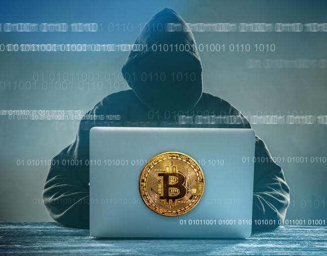 A person in a dark hoodie uses a laptop to buy Bitcoin on Coinmama; binary code flows.