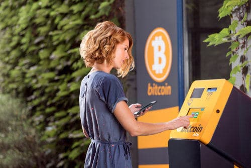 A person uses a Bitcoin ATM near greenery to buy crypto effortlessly via Coinmama.