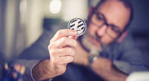 A man examines a BTC coin, contemplating whether to buy crypto on Coinmama.
