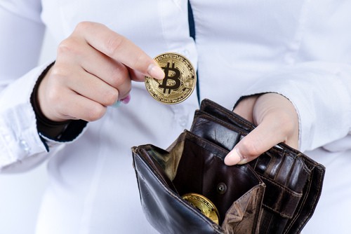 A person places a gold Bitcoin coin into a wallet, ready to buy crypto on Coinmama.
