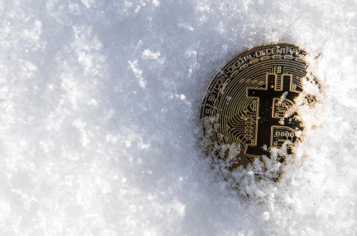 A partially buried Bitcoin in snow highlights Coinmama as a platform to buy BTC.